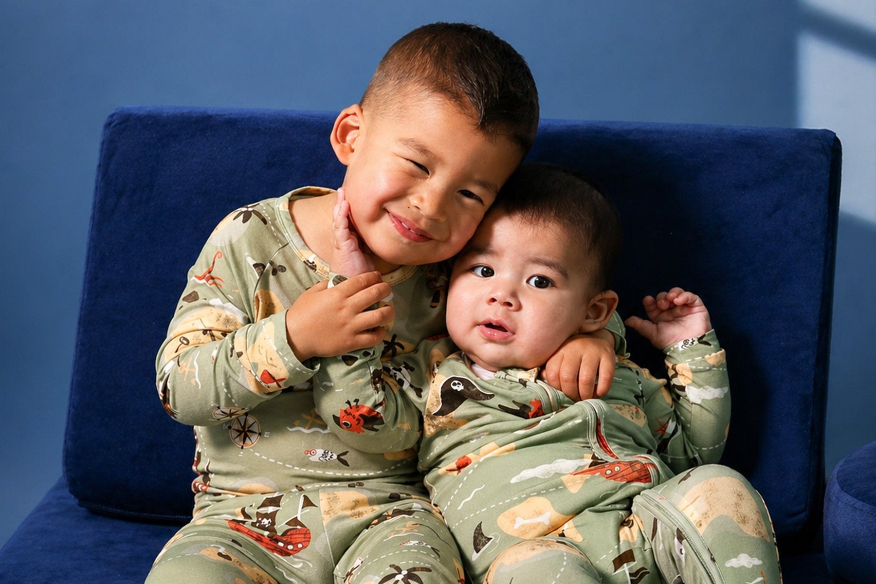 Two boys in matching Atlas & Maya Pirate Map bamboo pajamas on a blue sofa